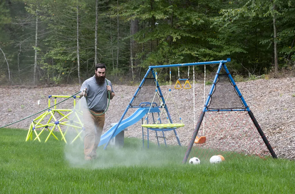 Zach Sarro spraying all-natural tick and mosquito control solution around swing set