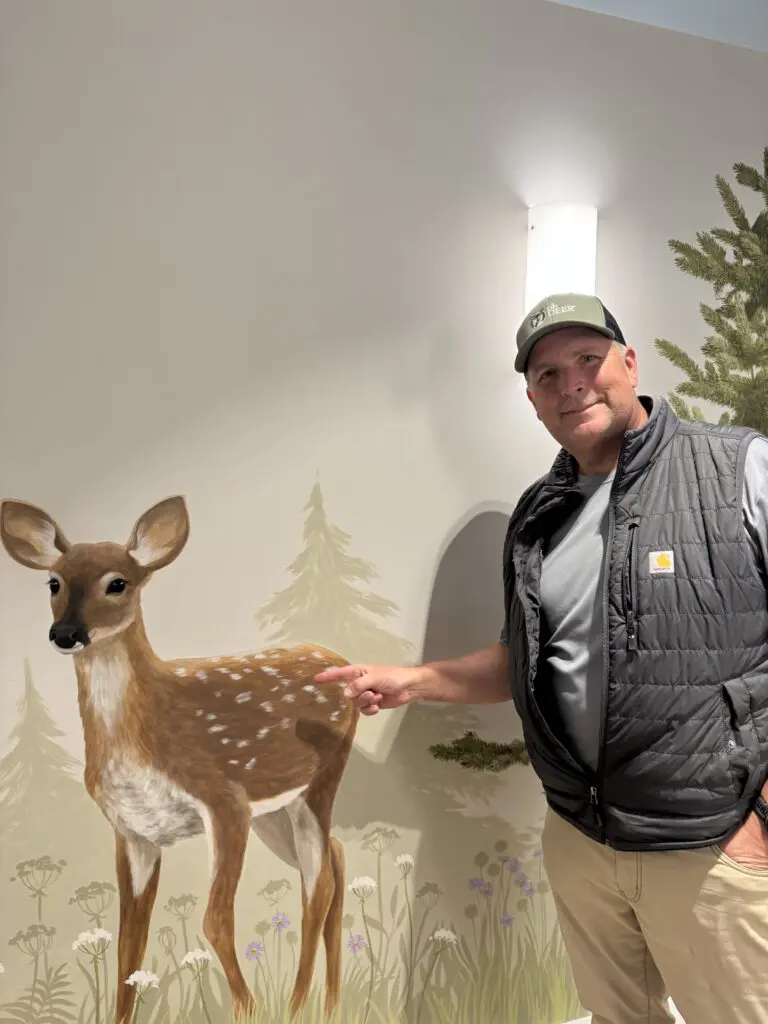 ohDEER founder Kurt Upham pointing to whitetail deer fawn painting 