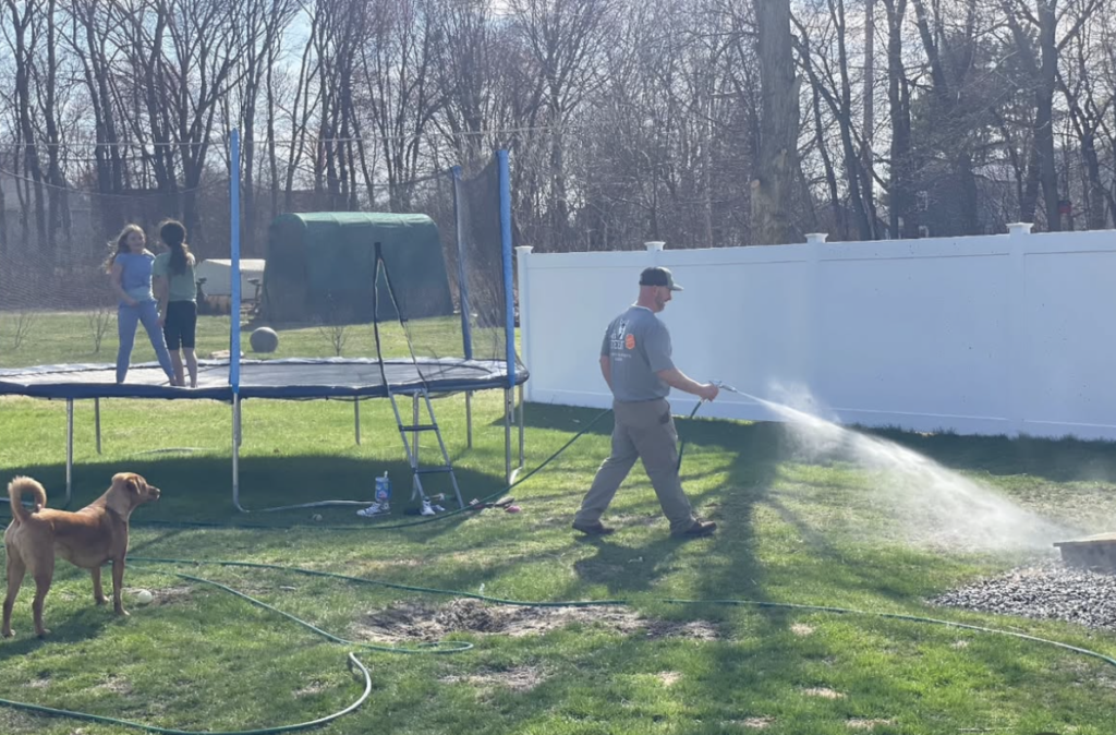 outdoor franchise opportunities owner of ohDEER Westford Nashua Steve Casello spraying all-natural tick & mosquito control in a yard with dog and kids playing on trampoline