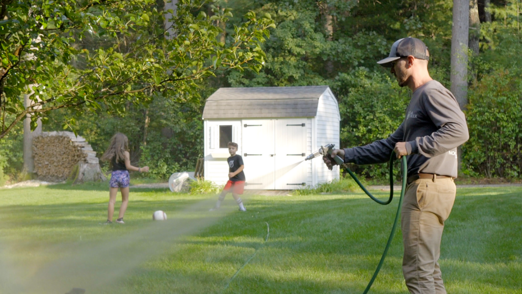outdoor franchise opportunities owner of ohDEER North Middlesex Bob Gaska spraying all-natural tick & mosquito control in a yard with kids playing soccer in the background