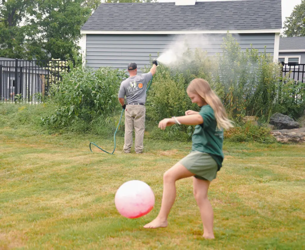 owner of ohDEER Westford Nashua Steve Casello spraying all-natural tick & mosquito control in a yard while girl kicks ball